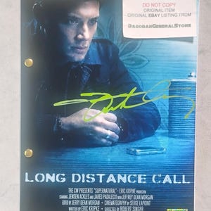 May include: A script cover for the Supernatural episode Long Distance Call, featuring a blue-toned image of Jensen Ackles, a bright green autograph, two gold fasteners, and text listing the cast and crew, with a white label in the top right corner.