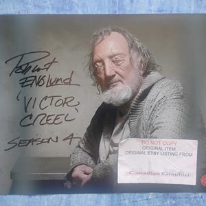 May include: A signed photograph of Robert Englund as 'Victor Creel' from Season 4. The image shows a close-up of Englund with a white beard and a grey sweater. The photo includes the text 'DO NOT COPY ORIGINAL ITEM ORIGINAL ETSY LISTING FROM Canadian Graphici'.