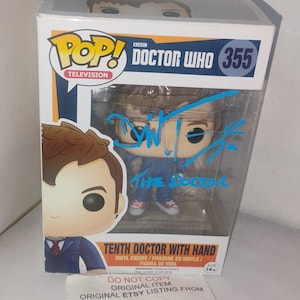 May include: A Funko Pop Television Doctor Who vinyl figure, number 355, titled Tenth Doctor with Hand. The box features a blue ink autograph across the clear plastic window. The packaging includes the text Pop, Doctor Who, and Tenth Doctor with Hand.