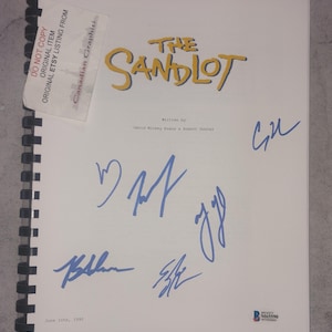 May include: A script for "The Sandlot" with the title in yellow and signatures in blue ink. The script is bound with a black spiral and includes text that reads "Written by David Mickey Evans & Robert Gunter."