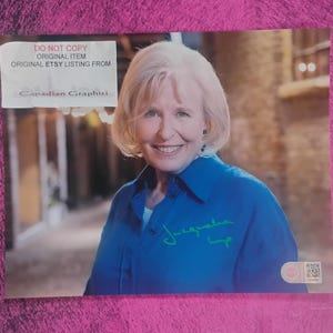 May include: A glossy photograph featuring a smiling person with blonde hair wearing a blue collared shirt. The image includes a green handwritten signature on the shirt, a white label with the text DO NOT COPY, and a small QR code sticker in the corner.