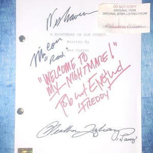May include: A white movie script page for A Nightmare on Elm Street written by Wes Craven. The page features black ink signatures and a pink ink inscription that reads Welcome to my nightmare! Robert Englund Freddy. Two metal fasteners are visible.