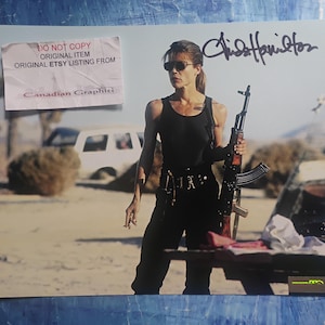 May include: A photograph featuring a woman in a black tank top and pants, holding a rifle. The image includes the text "DO NOT COPY ORIGINAL ITEM ORIGINAL ETSY LISTING FROM Canadian Graphiti" and a signature.