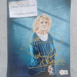 Peut inclure: Photographie signée d'une femme aux cheveux blonds bouclés, vêtue d'un haut bleu avec un sous-vêtement blanc. La signature est à l'encre dorée. Un autocollant dans le coin supérieur gauche indique "DO NOT COPY ORIGINAL ITEM ORIGINAL ETSY LISTING FROM Canadian Graphiti."