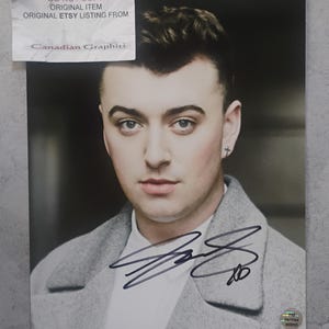 May include: A portrait of a person with short, dark hair, wearing a gray coat over a white shirt. The image includes an autograph and a sticker that reads "Certified Authentic". A sticker at the top reads "DO NOT COPY ORIGINAL ITEM ORIGINAL ETSY LISTING FROM Canadian Graphiti".