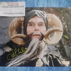 Op de afbeelding: Een portret van een persoon met grote, gebogen hoorns, een lange witte baard en een zwarte capuchon. De afbeelding heeft een handtekening in gouden inkt en een sticker met de tekst "DO NOT COPY ORIGINAL ITEM ORIGINAL ETSY LISTING FROM Canadian Graphiti."