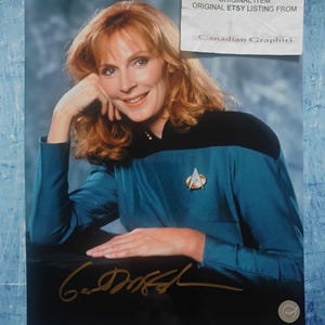 May include: A photograph of a woman with red hair, wearing a teal uniform with a black collar and a gold emblem. The image includes a signature and a sticker that reads "DO NOT COPY ORIGINAL ITEM ORIGINAL ETSY LISTING FROM Canadian Graphiti."
