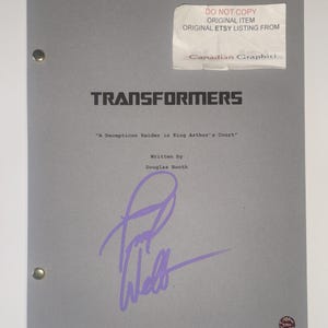 May include: A grey script titled Transformers: A Decepticon Raider in King Arthur's Court, written by Douglas Booth. The cover features a purple ink signature, two metal fasteners on the left side, and a white label with text at the top right.