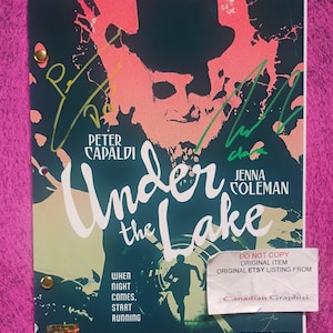 Pode incluir: Um roteiro de Doctor Who intitulado Under the Lake com Peter Capaldi e Jenna Coleman. A capa exibe uma silhueta escura contra um fundo azul-petróleo e coral com duas assinaturas distintas em tinta dourada e verde. Dois prendedores dourados prendem as páginas.