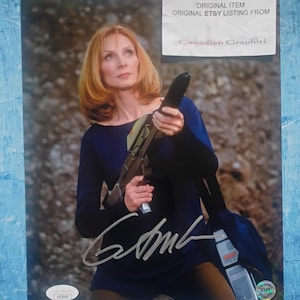 May include: A signed photograph featuring a woman with auburn hair, wearing a dark blue long-sleeved top and holding a futuristic weapon. The image includes the text "DO NOT COPY ORIGINAL ITEM ORIGINAL ETSY LISTING FROM Canadian Graphici."