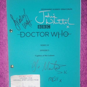 Pode incluir: Um roteiro turquesa de Doctor Who para a série 12, episódio 5, Fugitive of the Judoon, com o logotipo da BBC e o número do programa DRAA715N/01. A capa inclui várias assinaturas manuscritas em tinta preta e um adesivo branco no canto.