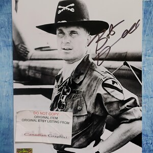 May include: Black and white photograph of a man in a military uniform and hat. The man is wearing a hat with a crossed sabers emblem. The photograph has an autograph and a sticker that reads "DO NOT COPY ORIGINAL ITEM ORIGINAL ETSY LISTING FROM Canadian Graphiti."