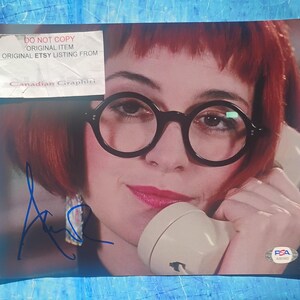May include: A photograph featuring a woman with red hair, wearing large, round black glasses, and holding a vintage telephone receiver. The image includes a signature and a sticker that reads "DO NOT COPY ORIGINAL ITEM ORIGINAL ETSY LISTING FROM Canadian Graphiti."