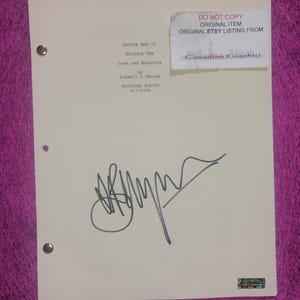 Pode incluir: Um roteiro de filmagem cor de creme para Doctor Who II, episódio dez, Love and Monsters, de Russell T Davies, datado de 8/3/2006. O documento apresenta uma assinatura em tinta preta, dois fechos metálicos no lado esquerdo e um adesivo.