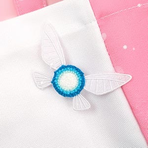 May include: White and blue fabric tote bag with a white embroidered design of a winged fairy with a blue and white centre.