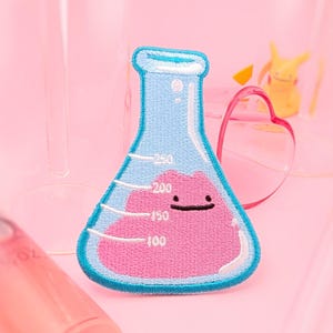 May include: A blue glass beaker with a pink, smiling blob inside. The beaker has markings for 100, 150, 200, and 250.