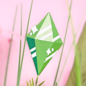 Puede incluir: Parche bordado verde en forma de diamante con rayas blancas y estrellas.