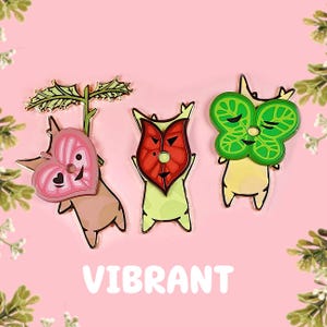May include: Three colorful enamel pins featuring characters from the video game "The Legend of Zelda: Majora's Mask". The pins are of a pink heart, a red mask, and a green leaf.