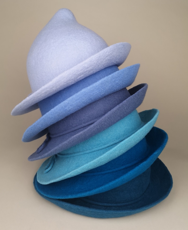 May include: A stack of six felt hats in shades of blue, from light to dark. The hats are all different shapes and sizes, and they are arranged in a gradient.