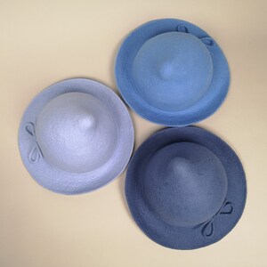 May include: Three felt hats in different shades of blue. The hats have a pointed crown and a wide brim. Each hat has a small bow on the side.