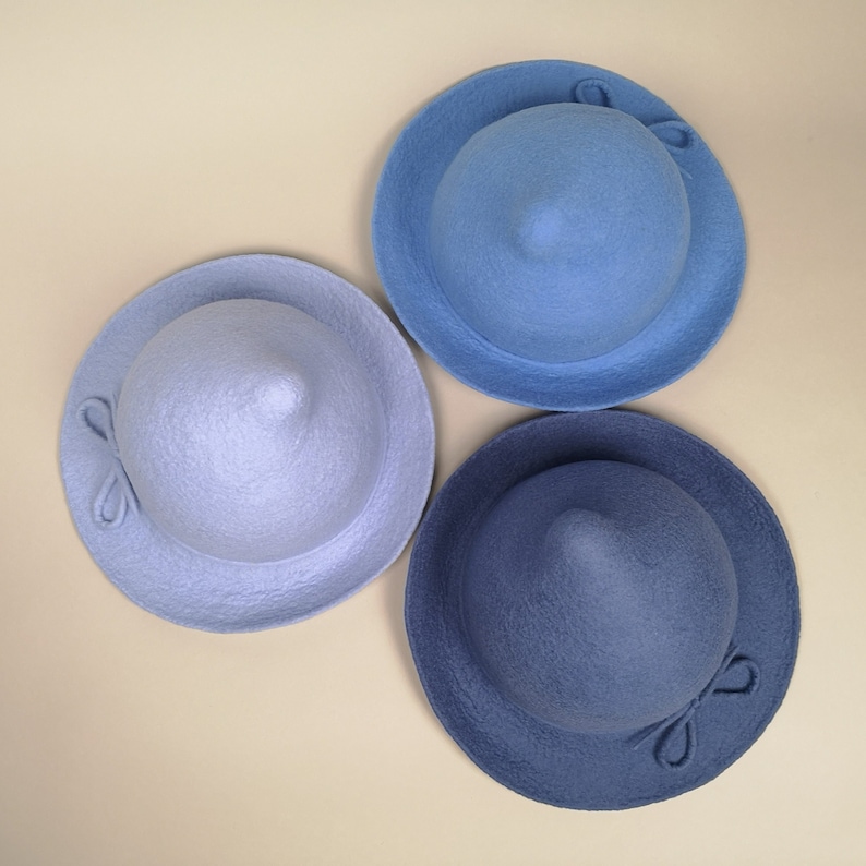 May include: Three felt hats in different shades of blue. The hats have a pointed crown and a wide brim. Each hat has a small bow on the side.
