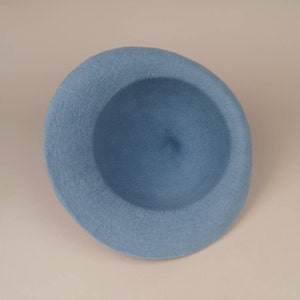 May include: A light blue felt beret hat. The hat is round and has a slightly indented crown.
