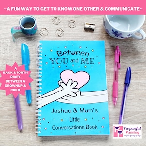 May include: A blue spiral bound journal with the title "Between You and Me" and a cartoon image of two hands holding a pink heart. The journal is labelled "Joshua & Mum's Little Conversations Book".