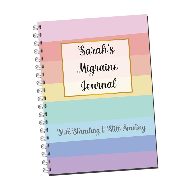 May include: A colorful spiral bound journal with the text "Sarah's Migraine Journal" in a gold frame and the text "Still Standing & Still Smiling" at the bottom.