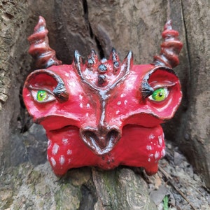 May include: A red and brown ceramic sculpture of a creature with large eyes and a textured surface. The creature has a pointed snout and two horns on its head.