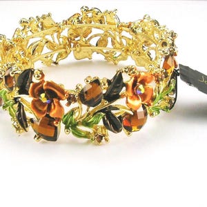 Könnte beinhalten: Goldfarbenes Armband mit Blumen- und Blattdesign. Das Armband hat orangefarbene und braune blütenförmige Edelsteine, grüne Blätter und kleine braune Edelsteine. Das Armband hat ein Etikett mit der Aufschrift "Joan Rivers".
