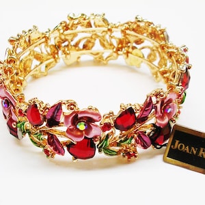 May include: Gold-tone bracelet with a floral design. The bracelet features red and pink gemstones and green enamel leaves. The tag reads "JOAN RIVERS".