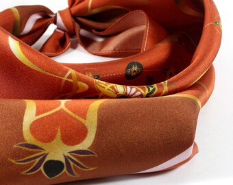 May include: A rust-colored silk scarf with a floral pattern. The scarf has a white border and is tied in a knot.