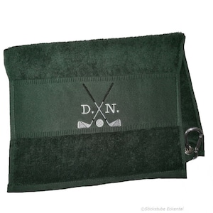 Könnte beinhalten: Ein dunkelgrünes Golftuch mit einem weißen gestickten Design aus zwei gekreuzten Golfschlägern, einem Golfball und den Initialen "D.N.". Das Handtuch hat eine Schlaufe zum Aufhängen.