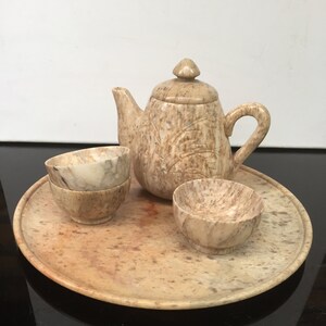 May include: A small, brown stone tea set with a teapot, two cups, and a tray. The set is made of a light brown stone with a speckled pattern.