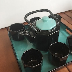 Könnte beinhalten: Eine schwarze Teekanne mit einem türkisfarbenen Deckel und einem schwarzen Griff, zusammen mit vier passenden schwarzen Teetassen, alles auf einem türkisfarbenen Tablett.