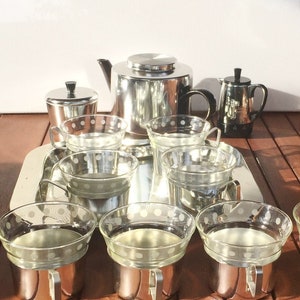 May include: A silver tea set with a teapot, creamer, sugar bowl, and six cups. The cups have a clear glass body with a silver rim and a white polka dot design.