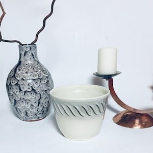 May include: A white ceramic planter with a grey rope design, a black and white speckled ceramic vase, and a copper candle holder with a white candle.
