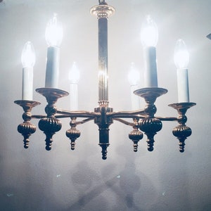 Könnte beinhalten: Ein goldfarbener Kronleuchter mit sechs Kerzenleuchten. Der Kronleuchter hat ein traditionelles Design mit verzierten Details.