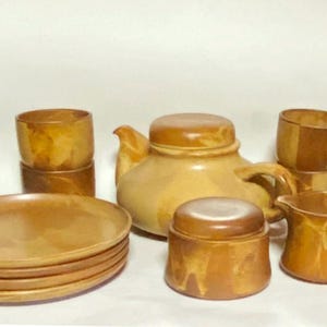 Könnte beinhalten: Ein braunes und beigefarbenes Keramik-Tee-Set mit einer Teekanne, einer Zuckerdose, einem Milchkännchen und vier Tassen. Das Set hat einen rustikalen, erdigen Look.
