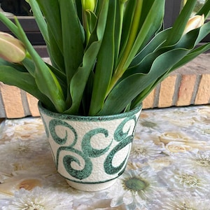 Może przedstawiać: Biała ceramiczna doniczka z zielonym wzorem w postaci spirali, wypełniona bukietem zielonych tulipanów.