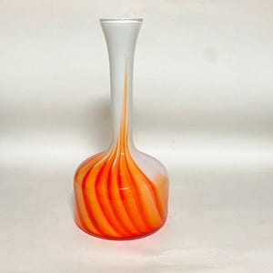 Könnte beinhalten: Eine dekorative Glasvase mit weißem Hals und rundem Boden. Der Boden hat ein orangefarbenes Wirbelmuster, das in den weißen Hals übergeht. Die Vase ist ein stilvolles Wohnaccessoire.