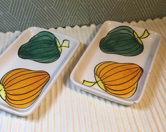 May include: Two rectangular ceramic serving dishes with a white background and painted green and orange gourds.