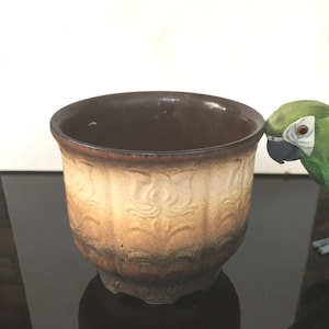 Peut inclure: Un pot en céramique brun et crème avec un motif en relief décoratif. Le pot a un fond arrondi et une large ouverture.