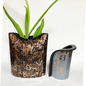 May include: Two ceramic vases with a curved design. The larger vase is black with gold and brown geometric patterns. The smaller vase is gray with gold accents.