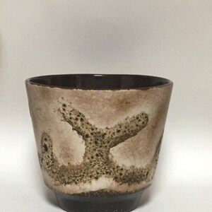 May include: A brown and white ceramic planter with a speckled glaze and a unique abstract design. The planter has a wide, round opening and a slightly flared lip.