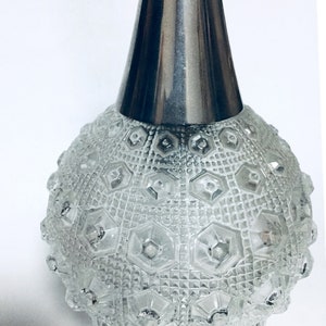 Może przedstawiać: Wisiorek lampy wykonany z przezroczystego szkła z fakturowanym, geometrycznym wzorem i srebrnym metalowym wierzchołkiem.