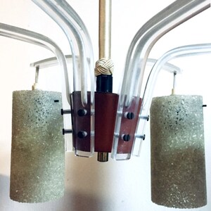 May include: A modern chandelier with six clear acrylic arms and three frosted glass cylinder shades. The chandelier has a brown wooden center piece with black screws.