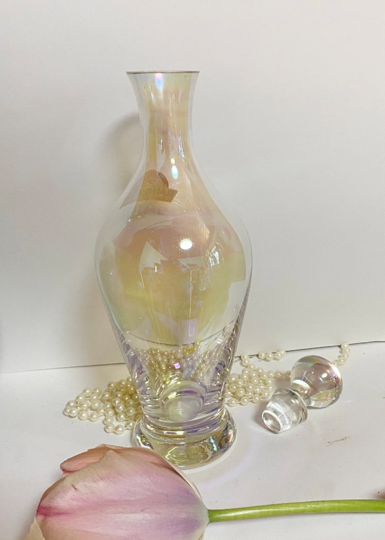 May include: A clear iridescent glass bottle with a wide base and a narrow neck. The bottle has a pearlescent finish and is perfect for displaying flowers or other decorative items.