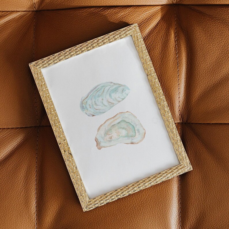 Puede incluir: Una pintura de acuarela enmarcada de dos conchas de ostra sobre un fondo blanco. Las conchas est&aacute;n pintadas en tonos de azul, verde y blanco.