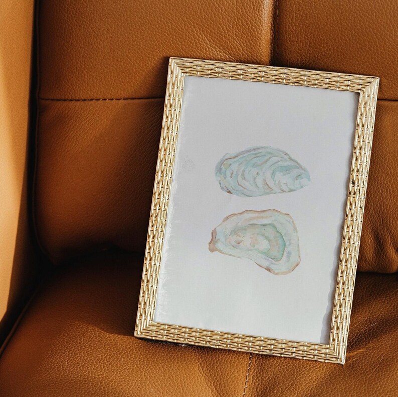 Puede incluir: Una pintura de acuarela enmarcada de dos conchas de ostra sobre un fondo blanco. Las conchas est&aacute;n pintadas en tonos de azul, verde y blanco.